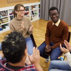 Multi-ethnic group of young people sitting in circle and clapping during class in college, copy space